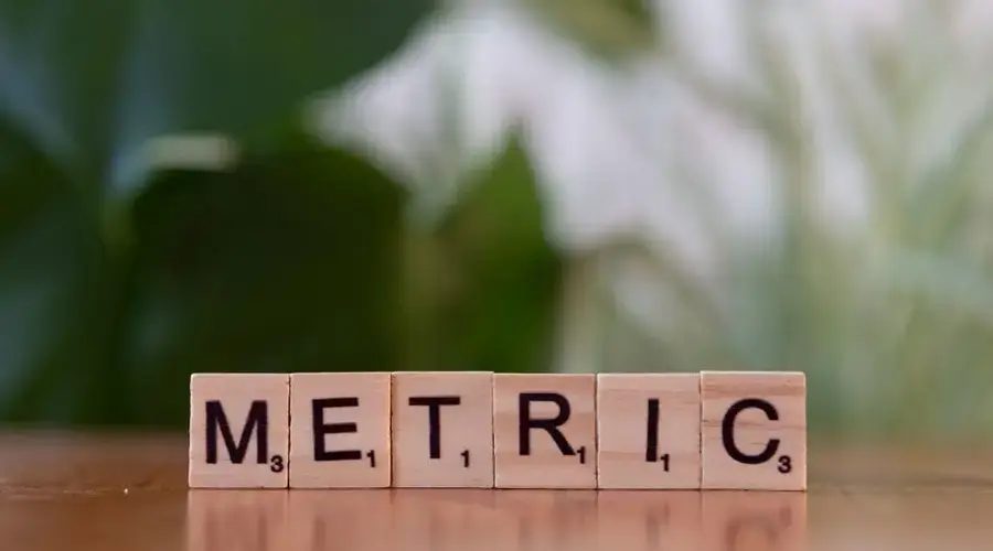 Close-up of wooden tiles spelling 'Metric' on a table, with a blurred green background.