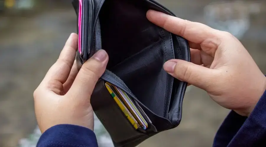 An outdoor image of hands holding an empty black wallet, suggesting financial scarcity.