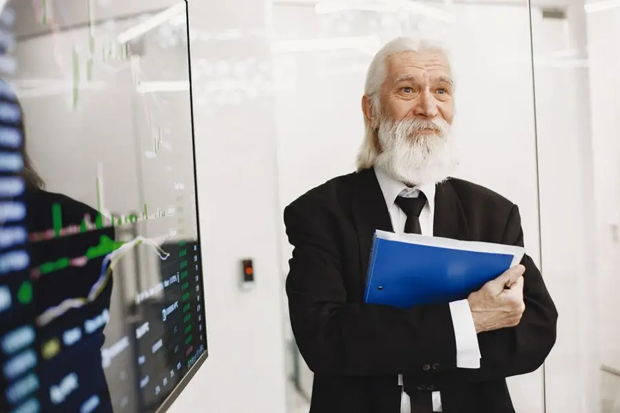 Elderly businessman in suit analyzing financial graphs in modern office.