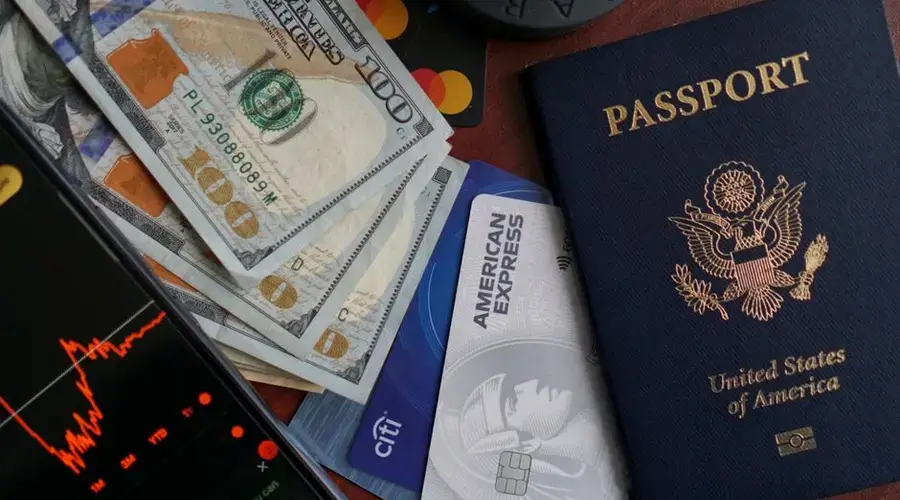 Top view of US passport, credit cards, cash, and phone showing financial graph, ideal for travel themes.