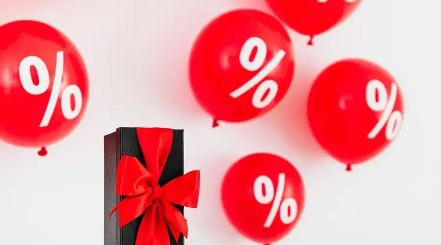 Stylish black gift box with red ribbon surrounded by red percentage balloons on a white background.