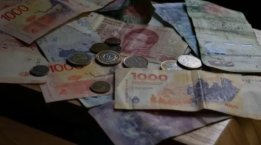 A collection of Argentine banknotes and coins displayed on a wooden table.