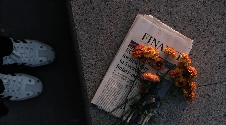 Yellow daisies placed on a financial newspaper on stone pavement during sunset.