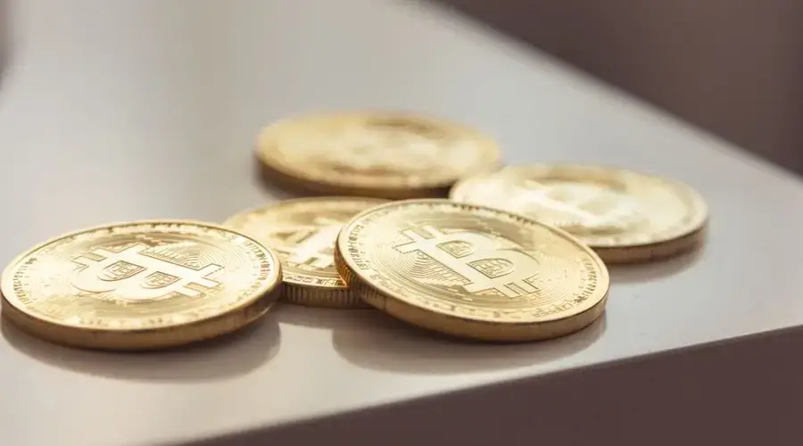 Close-up of shiny gold Bitcoin coins on white surface, symbolizing cryptocurrency wealth.