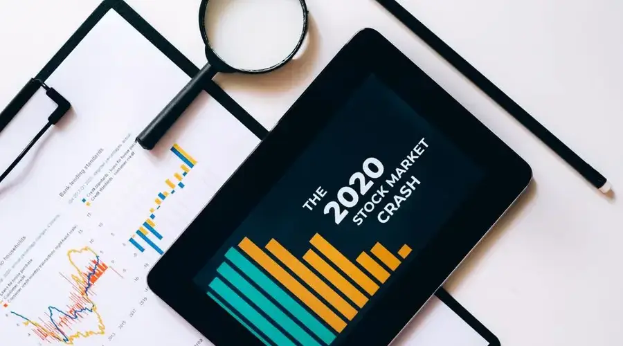 Magnifying glass and tablet analyze 2020 stock market crash data with charts on clipboard.