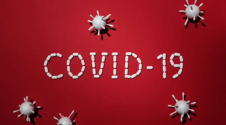 Artistic representation of COVID-19 using pills and virus models on red background.