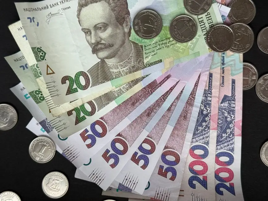 Close-up of assorted Ukrainian banknotes and coins on a dark background.