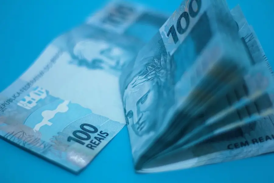 Stack of 100 Brazilian real notes placed on a blue surface, showcasing currency details.