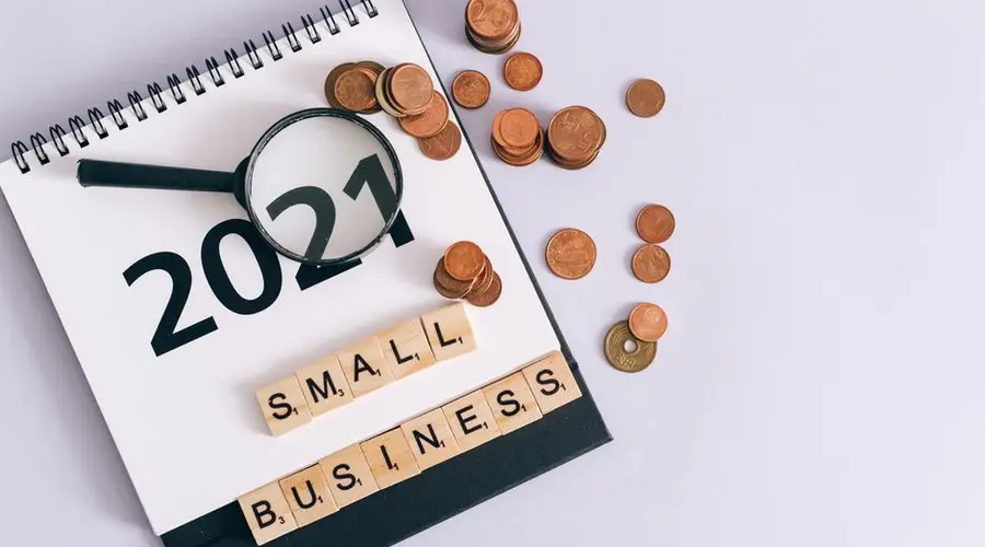 Flat lay of 2021 calendar, coins, magnifying glass, and 'small business' scrabble tiles.