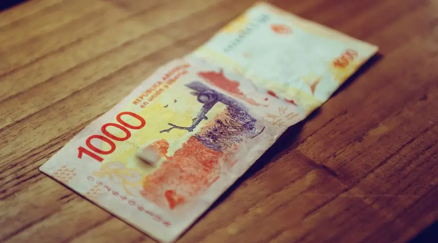 Close-up of 1000 Argentine peso banknote displayed on a wooden table, focusing on currency details.