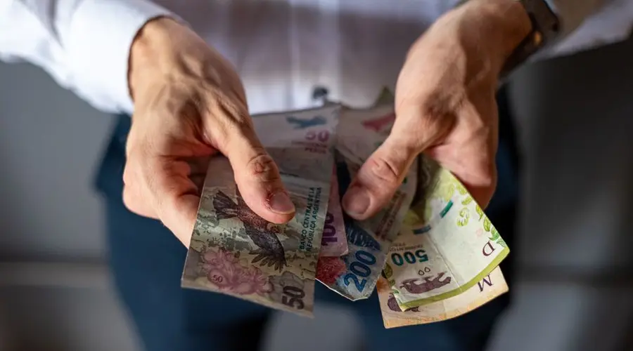 Closeup of hands holding various Argentine peso banknotes, depicting economic and financial concepts.
