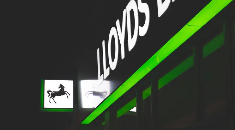 Bright green and white neon signs of Lloyds Bank against a dark night sky.