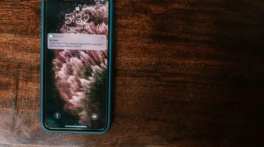 Close-up of smartphone on wooden surface displaying a bank alert message.