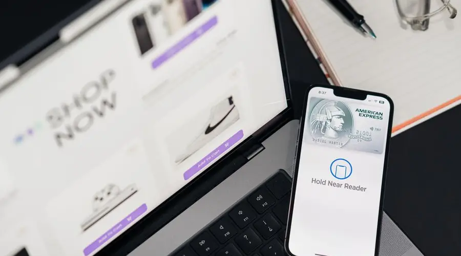 Smartphone with payment terminal app next to laptop displaying online shopping site.