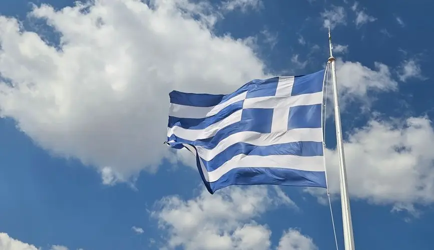 A Greek flag waves against a vibrant blue sky in Athens, Greece.