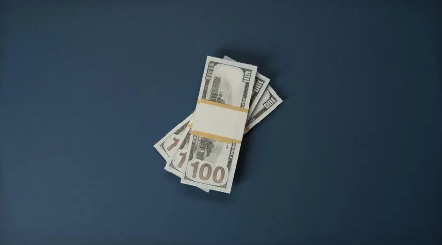 Stack of 100 US dollar bills on a dark surface, symbolizing wealth and finance.