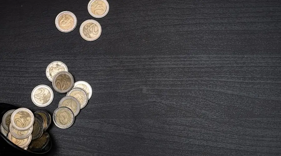 A collection of euro coins scattered on a dark textured surface, with space for text.