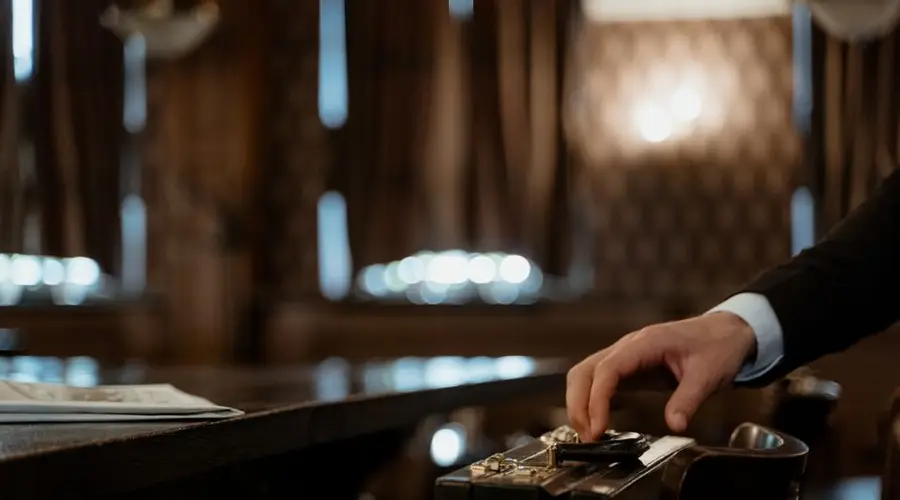 A close-up shot captures a hand holding a black briefcase in a dimly lit elegant room with a blurred background.