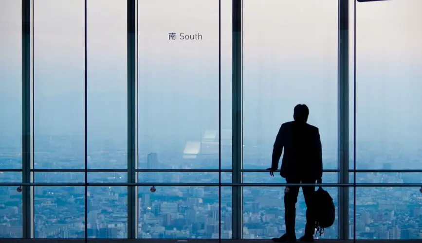 A lone businessman overlooking the city from a high-rise building during day.