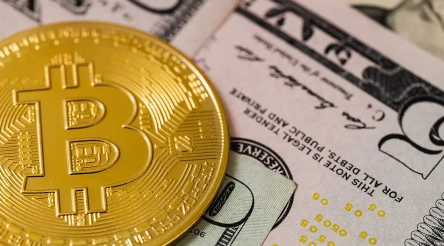 Close-up of a Bitcoin coin placed on US dollar bills, depicting cryptocurrency and traditional currency.