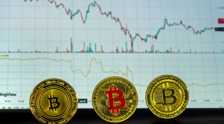 Three Bitcoin coins in front of a financial trading graph depicting market trends and analysis.