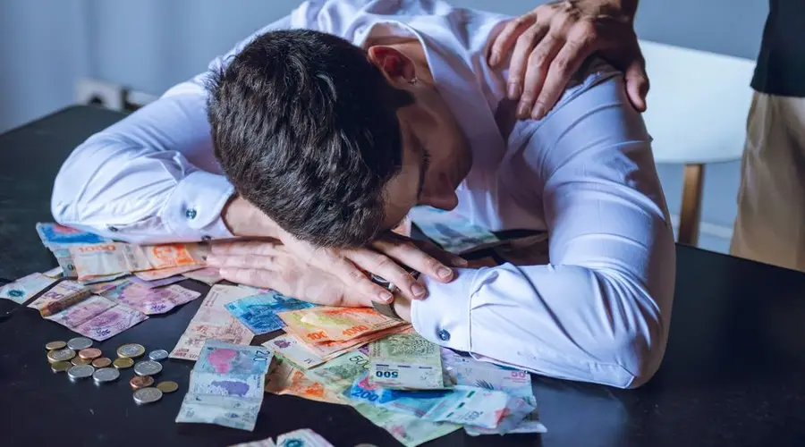 A man is overwhelmed with Argentine pesos, reflecting financial stress and support from another person.