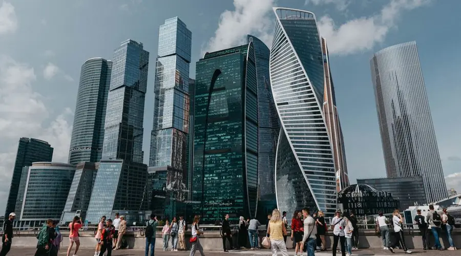 Diverse crowd stands in front of iconic modern skyscrapers in a vibrant cityscape.
