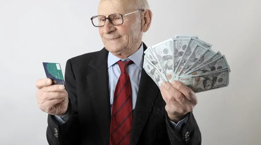 Elderly man in a suit holding a credit card and US dollar bills, representing finance and wealth.