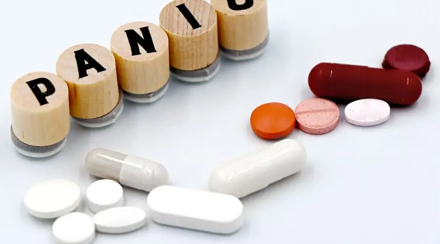 Assorted pills arranged beside wooden tiles spelling 'PANIC', symbolizing anxiety treatment.