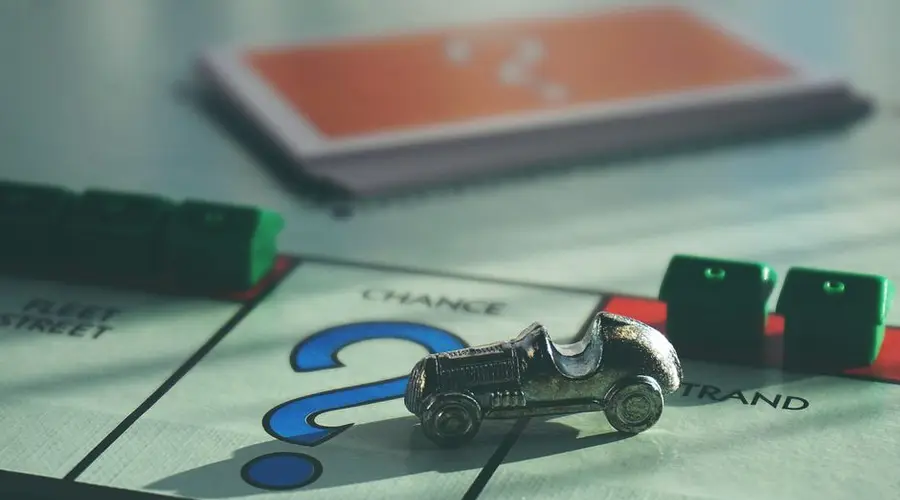 A close-up of a Monopoly board game featuring a silver car token and chance card.