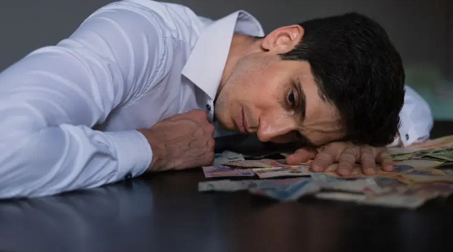 Adult man in white shirt resting on Argentine currency, showing financial stress.