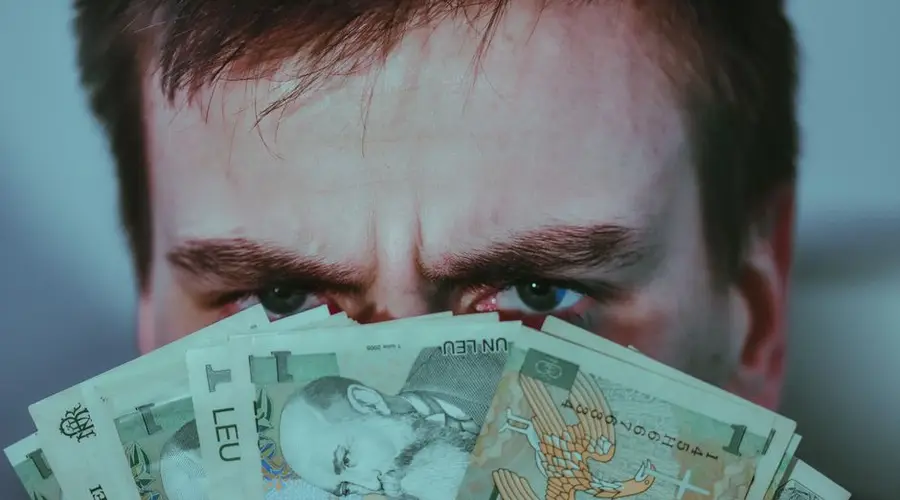 Crop unrecognizable frown man with dark hair covering face with stack of Romanian leu banknotes and looking at camera