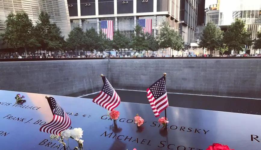 A poignant tribute at the 9/11 Memorial in NYC with flags and flowers honoring victims.