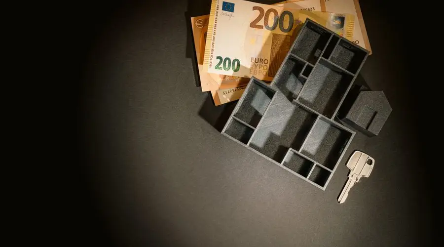 A top view of euro banknotes, a miniature architectural model, and a key symbolizing property investment.