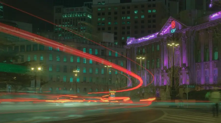 Dynamic city night scene with colorful light trails in front of illuminated buildings.