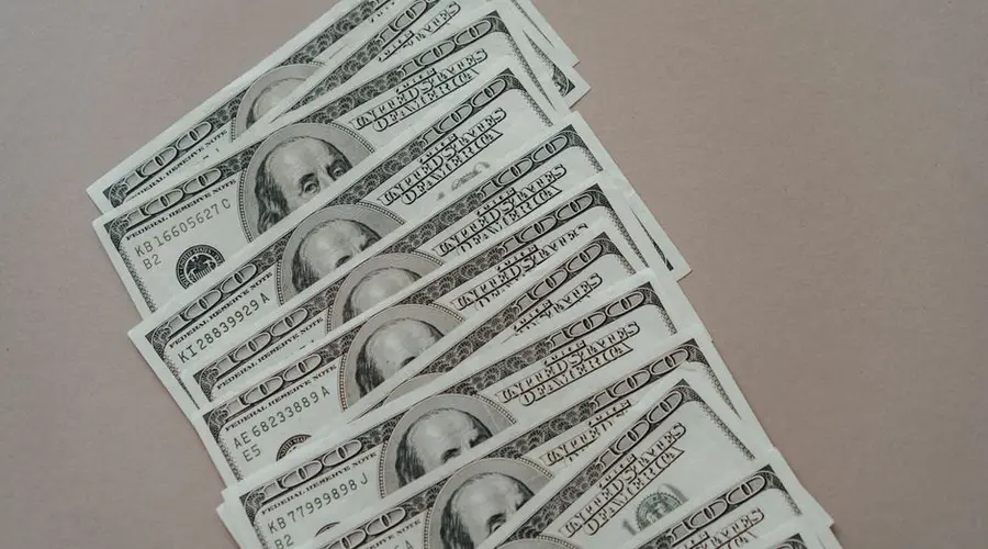 A close-up of multiple US dollar bills arranged on a neutral surface.