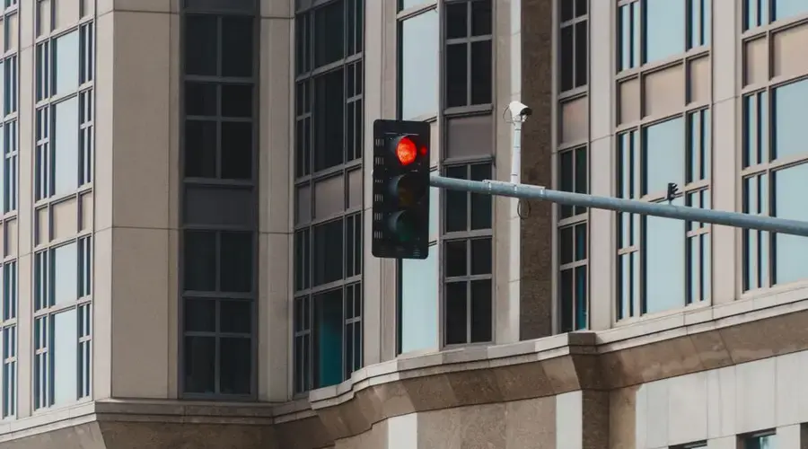 Red traffic light in cityscape setting with modern glass building facade.