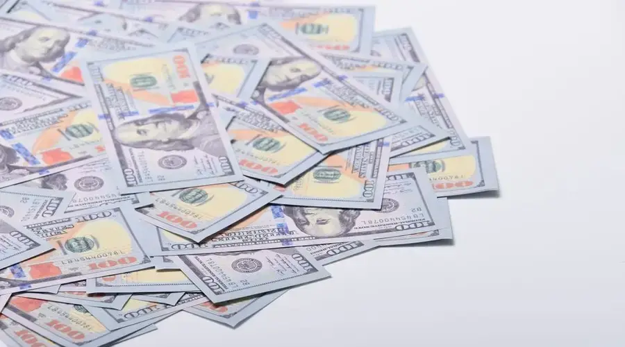 A scattered pile of US hundred dollar bills on a clean white surface.