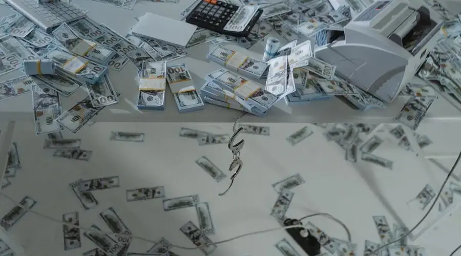 Stacks of US dollar bills scattered across a desk with a money counter and calculator.