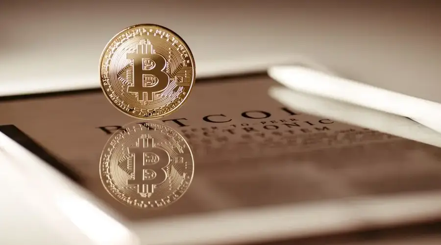 Close-up of a gold Bitcoin reflecting on a digital tablet screen, showcasing cryptocurrency concepts.
