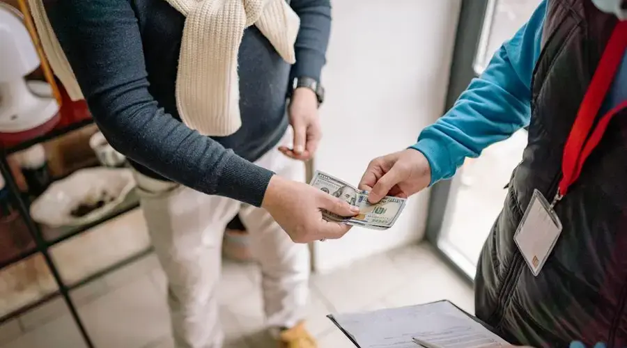 Close-up of hands exchanging cash during a transaction indoors, highlighting payment details.