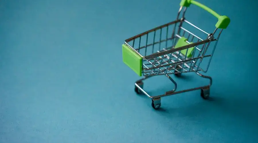 A miniature shopping cart with green accents on a blue background, perfect for retail concepts.