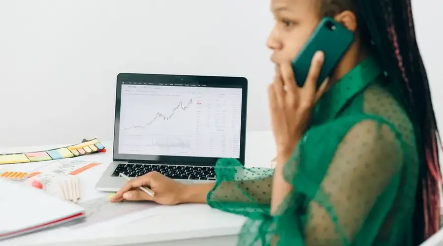 African American woman reviewing stock market charts on a laptop while talking on the phone.