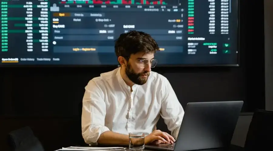 Professional analyzing stock market trends using laptop and digital display in modern office.