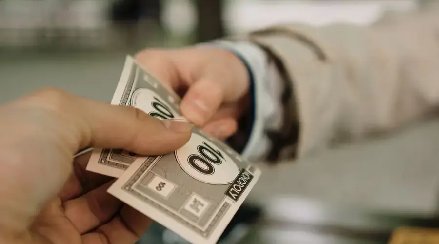 Close-up of two hands exchanging Monopoly money, symbolizing a financial transaction.