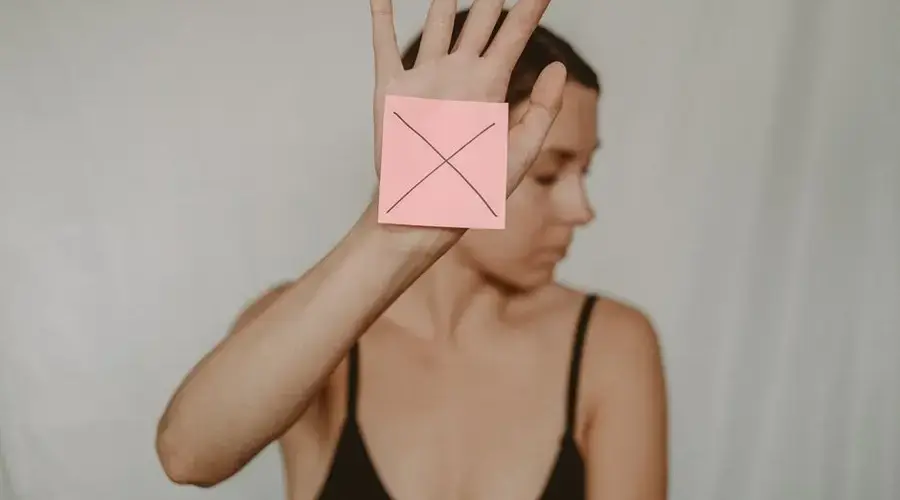Young slender woman with closed eyes demonstrating sign stop with sticker on palm