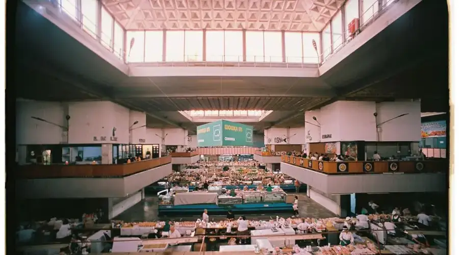 Vibrant indoor market scene in a geometric architectural setting with diverse stalls and busy activity.