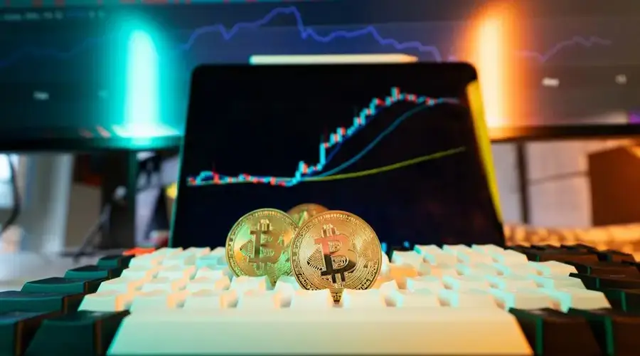 Close-up of Bitcoin coins on a keyboard with a trading chart in the background