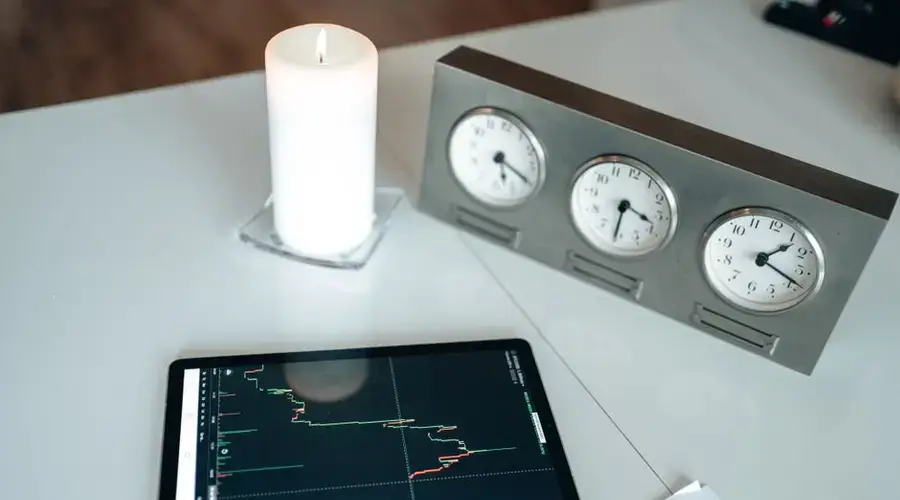 Tablet displaying stock market data on a desk with a candle and world clocks, symbolizing global trading.