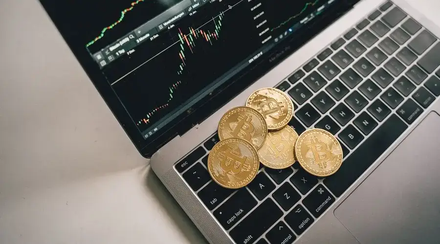 Golden bitcoin coins placed on a laptop keyboard with trading chart displayed on the screen.